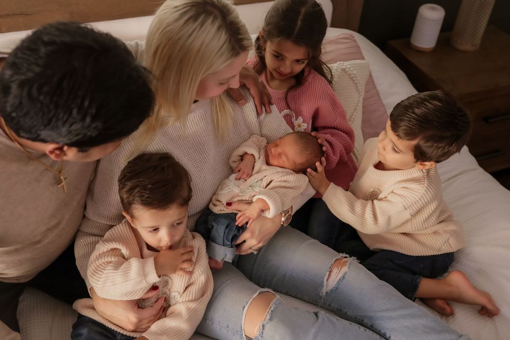 Family of six with parents and four children gathered on a bed admiring their newborn baby.