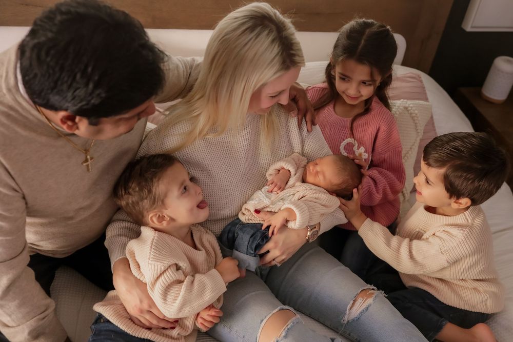 Family with four children gathered on a bed admiring their newborn baby.