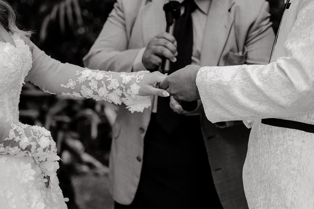 Black and white photo of bride and groom exchanging rings at wedding.