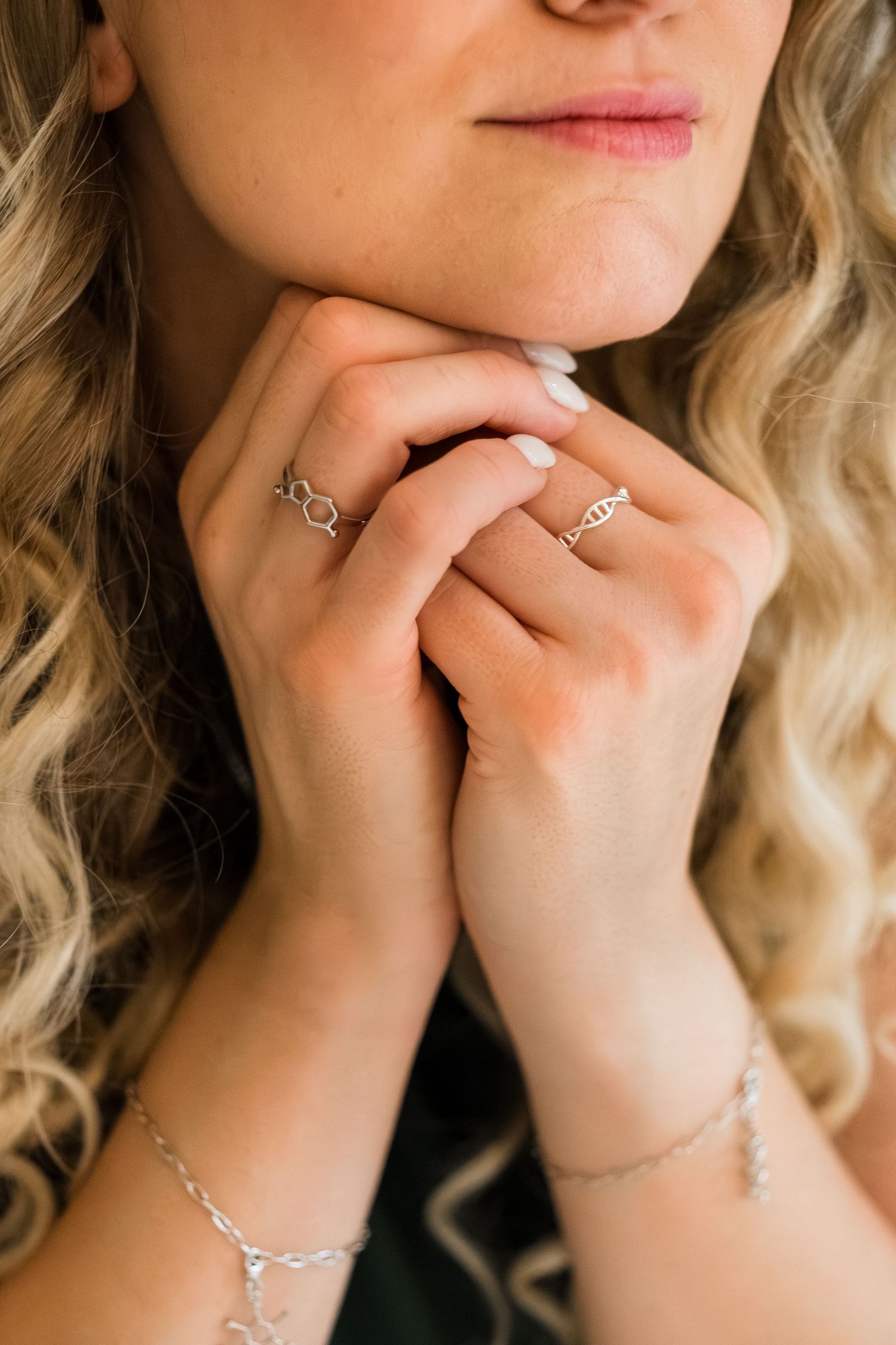 Close-up of a woman's hands adorned with delicate silver rings and a chain bracelet, with curly blonde hair.