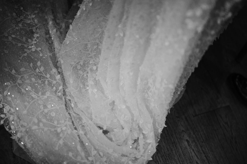 Close-up black and white detail shot of delicate beaded lace wedding dress fabric.