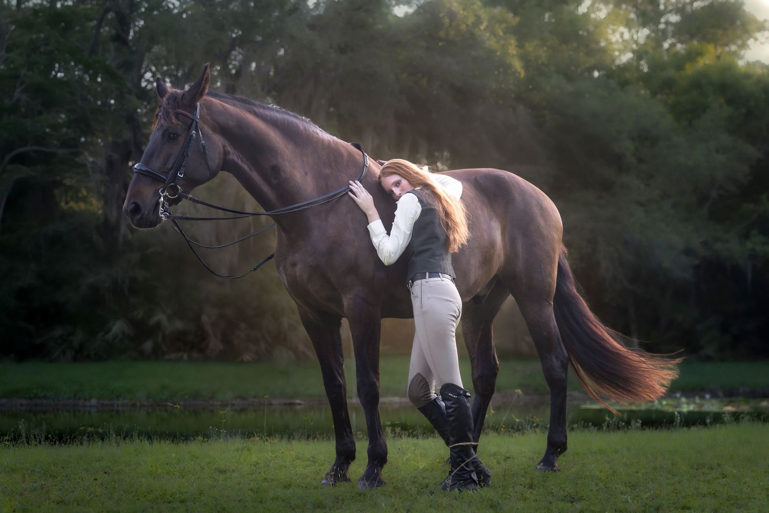 Woman in equestrian attire leaning affectionately against a dark brown horse in a green meadow.