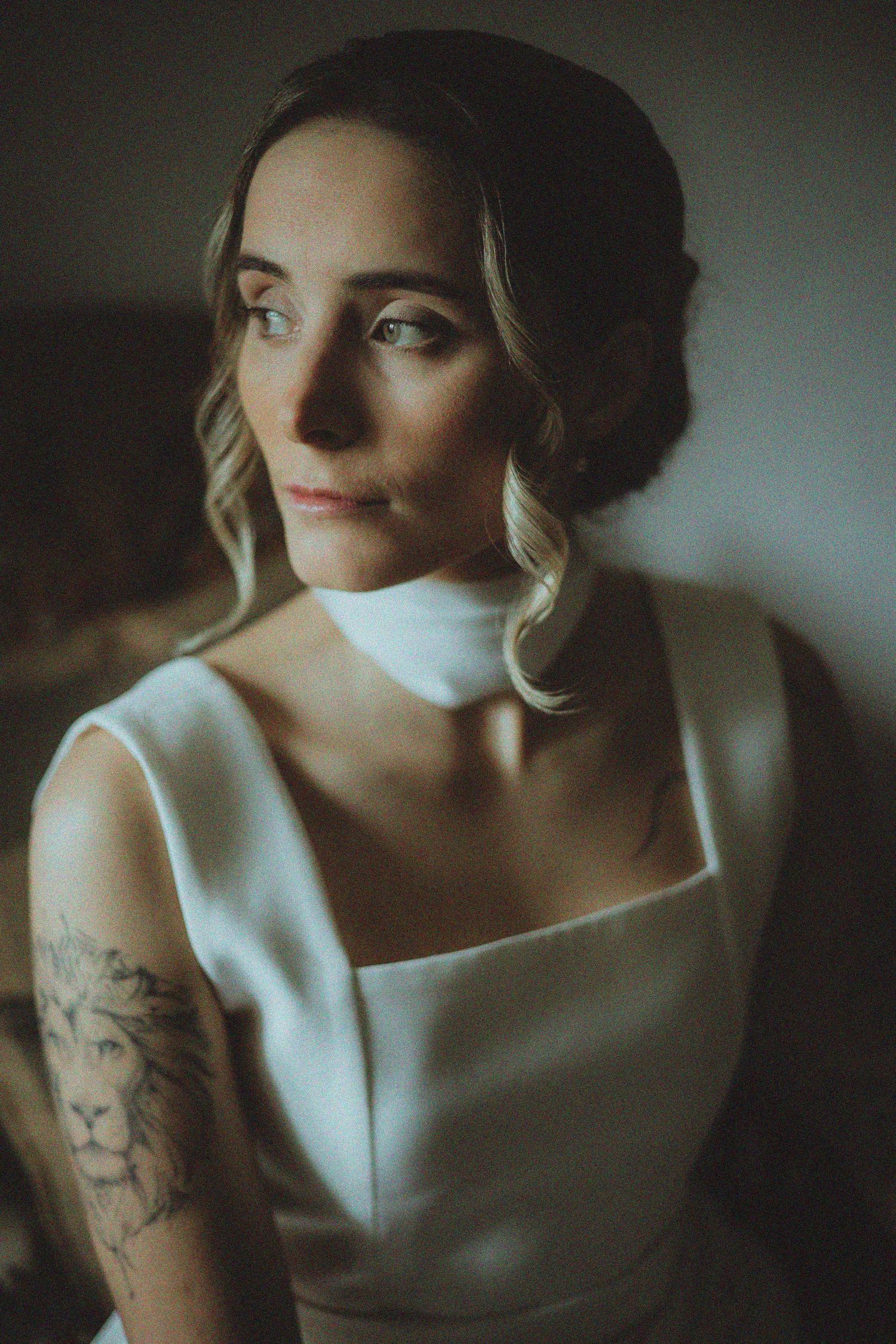 Artistic portrait showing white dress and tattoo in moody lighting.
