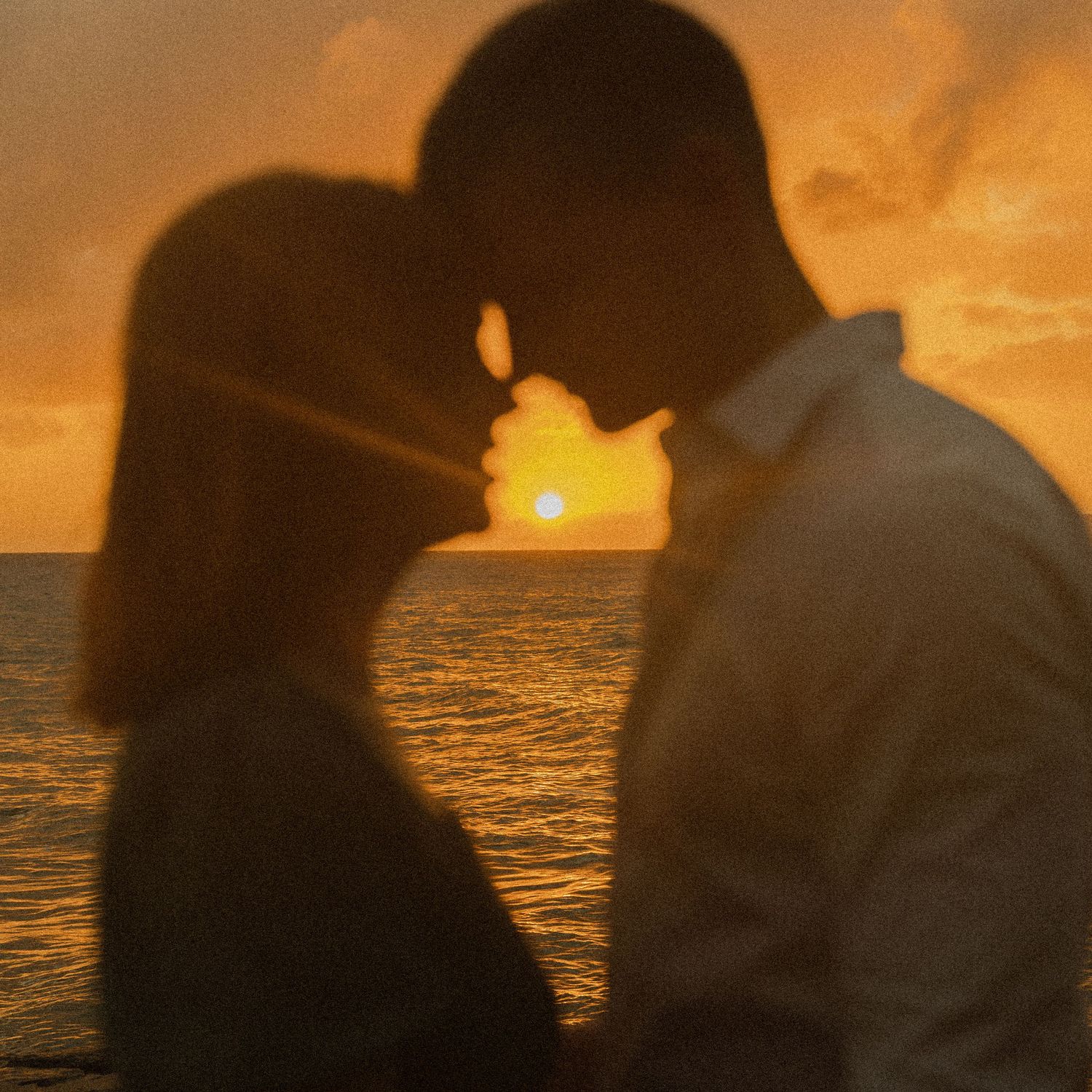 Silhouetted couple sharing intimate moment against dramatic ocean sunset.