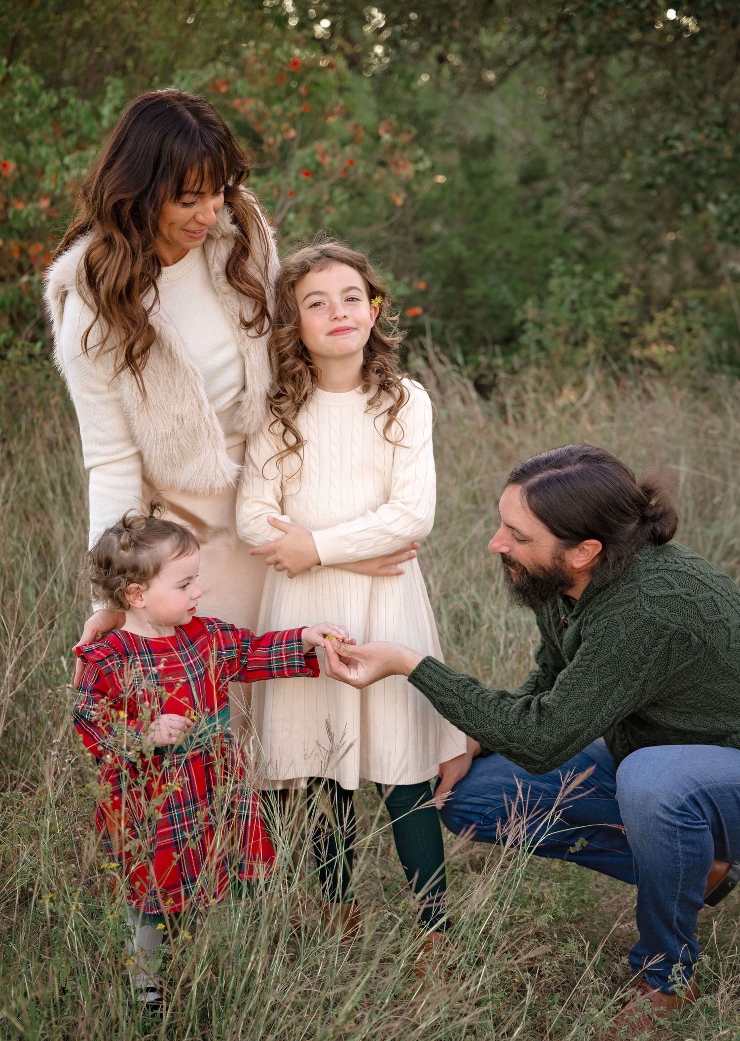 A family shares tender moments together while sitting in a field of tall grass during an outdoor photo session.