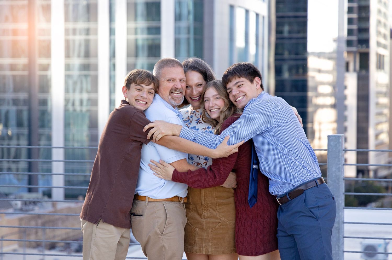 Group of people hugging and laughing together outdoors with modern office buildings in the background.