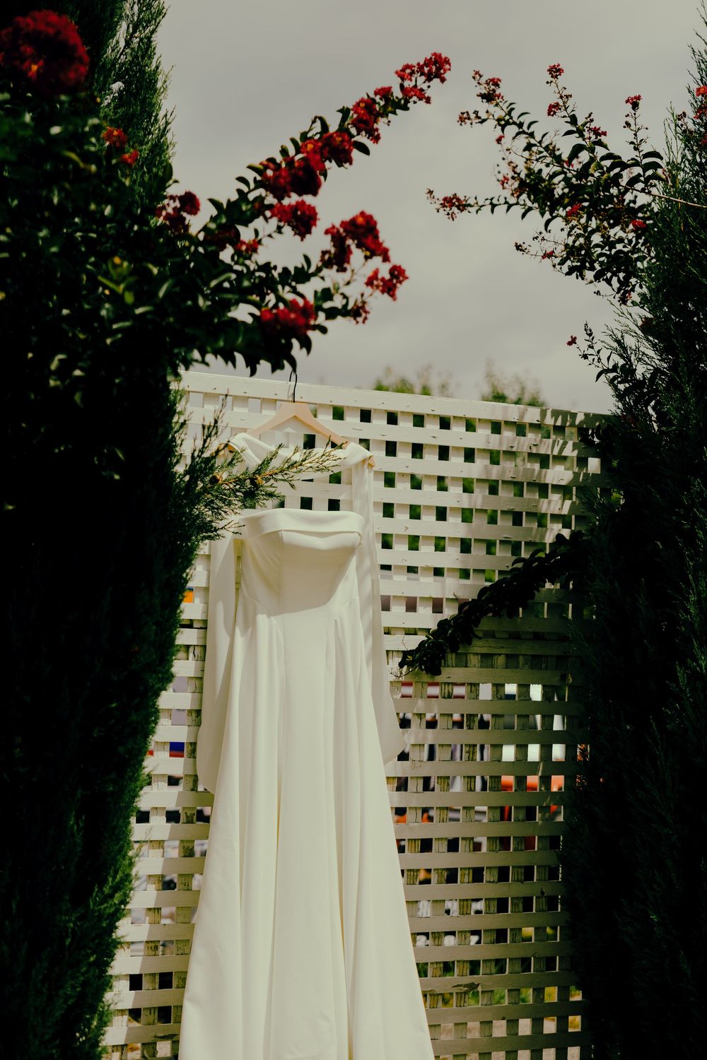 Bride's dress hanging on a fence near florals in a garden.
