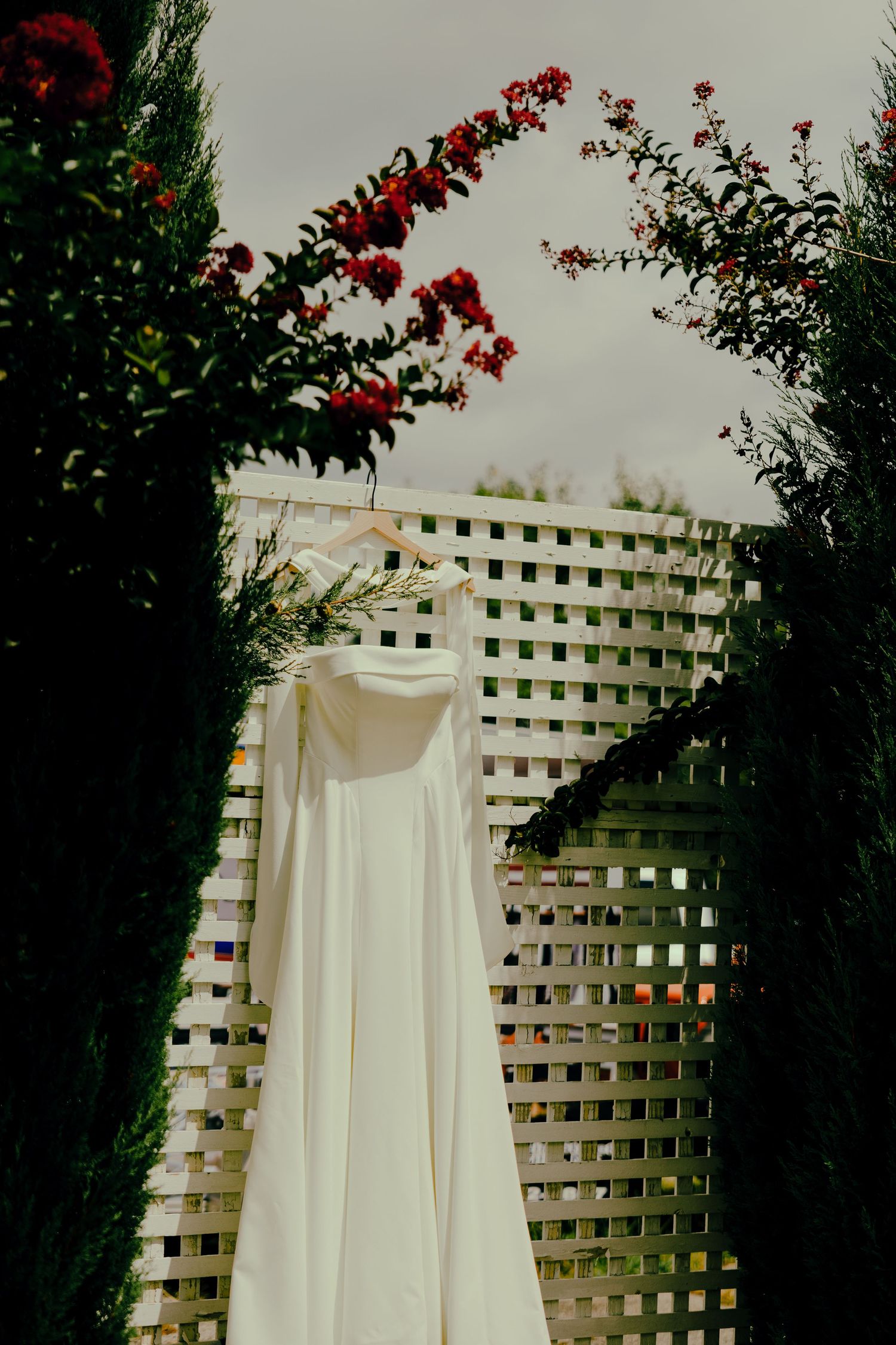 Bride's dress hanging on a fence near florals in a garden.