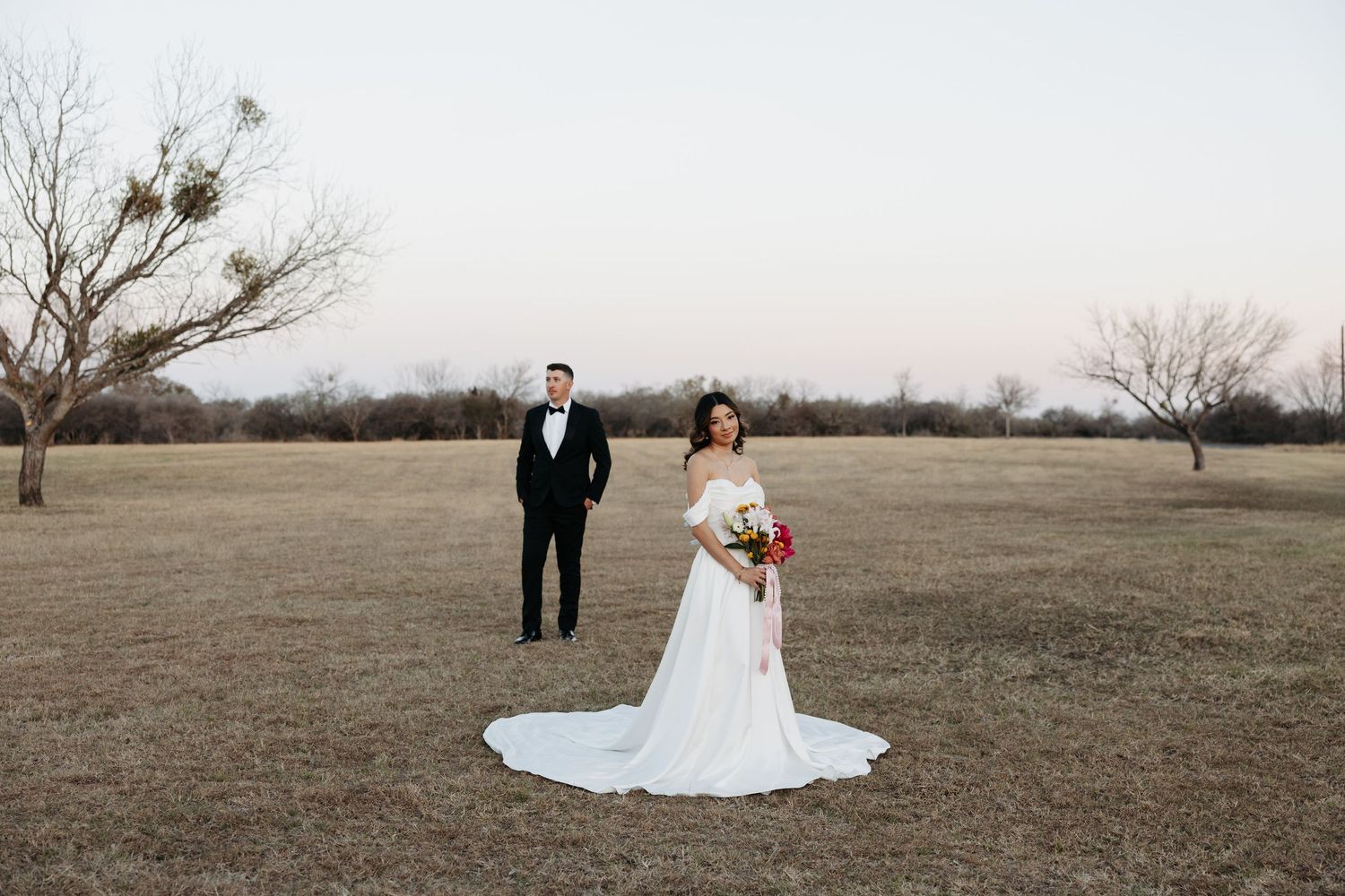 A couple shares romantic moments at an elegant brick building entrance with arched doorways and white columns.