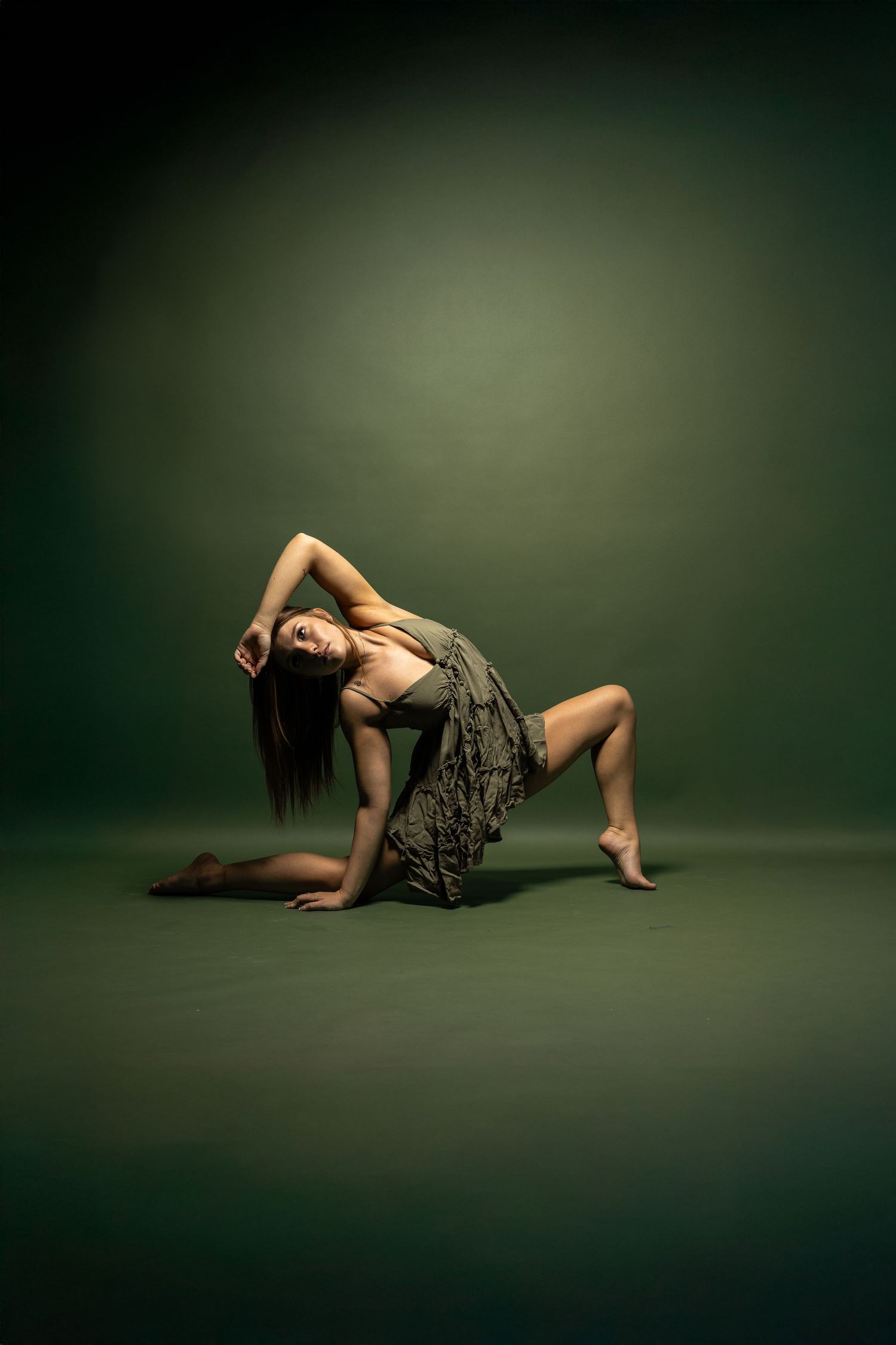 Dancer in flowing dark dress performs expressive floor movement against dark green backdrop. West Michigan.