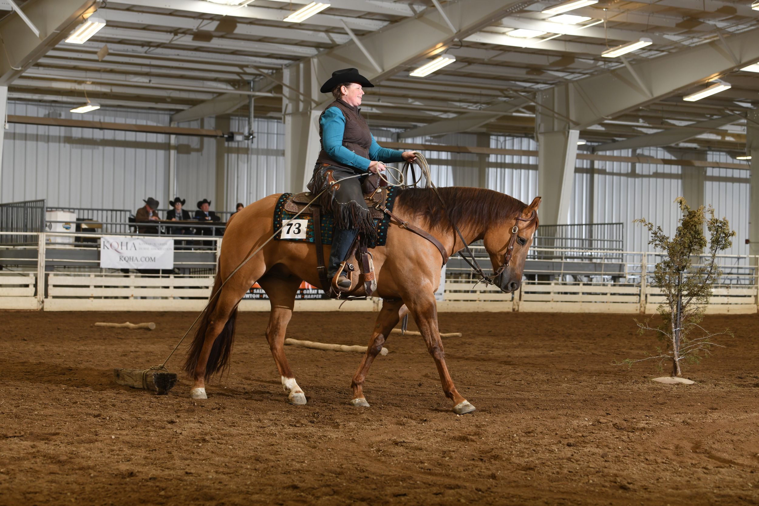 Western horse and rider navigate through competition pattern in indoor arena.
