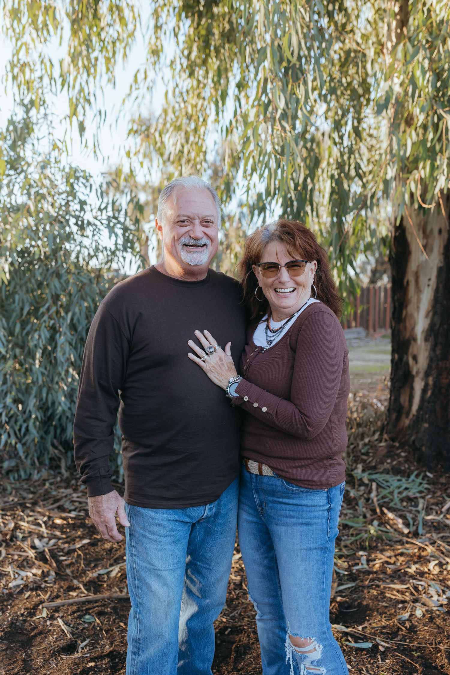a older couple standing outdoors near a tree embracing and smiling