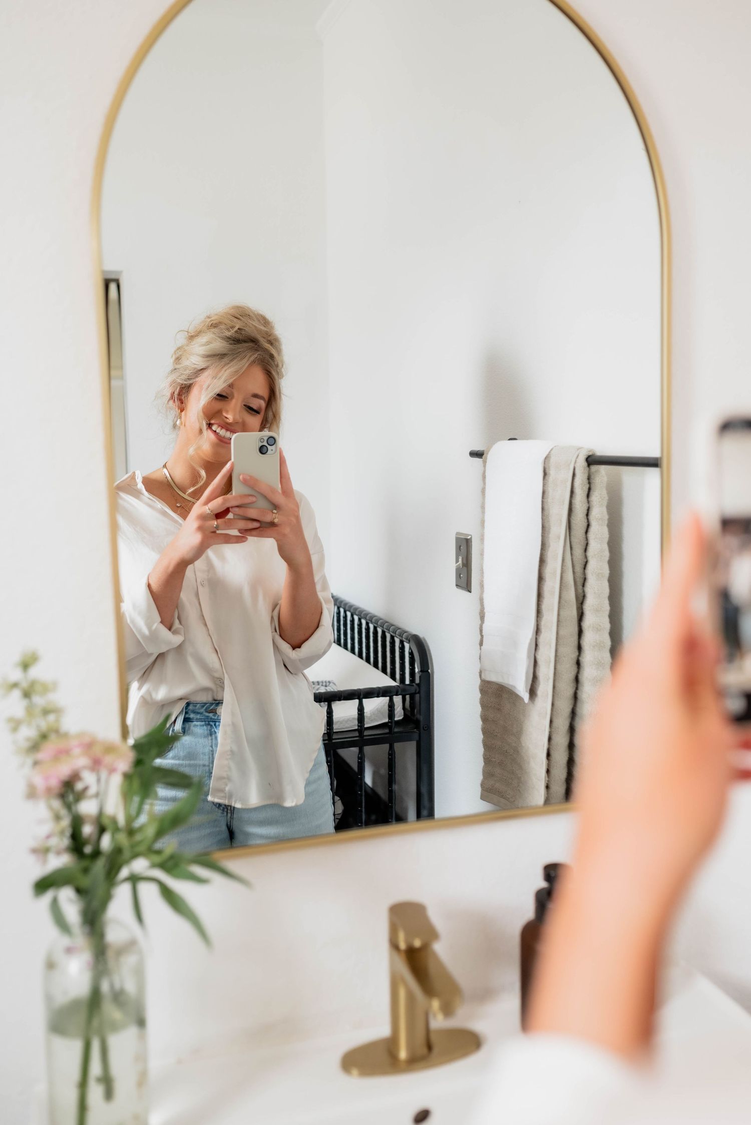 Mirror selfie in modern bathroom with arched gold frame mirror and white decor.