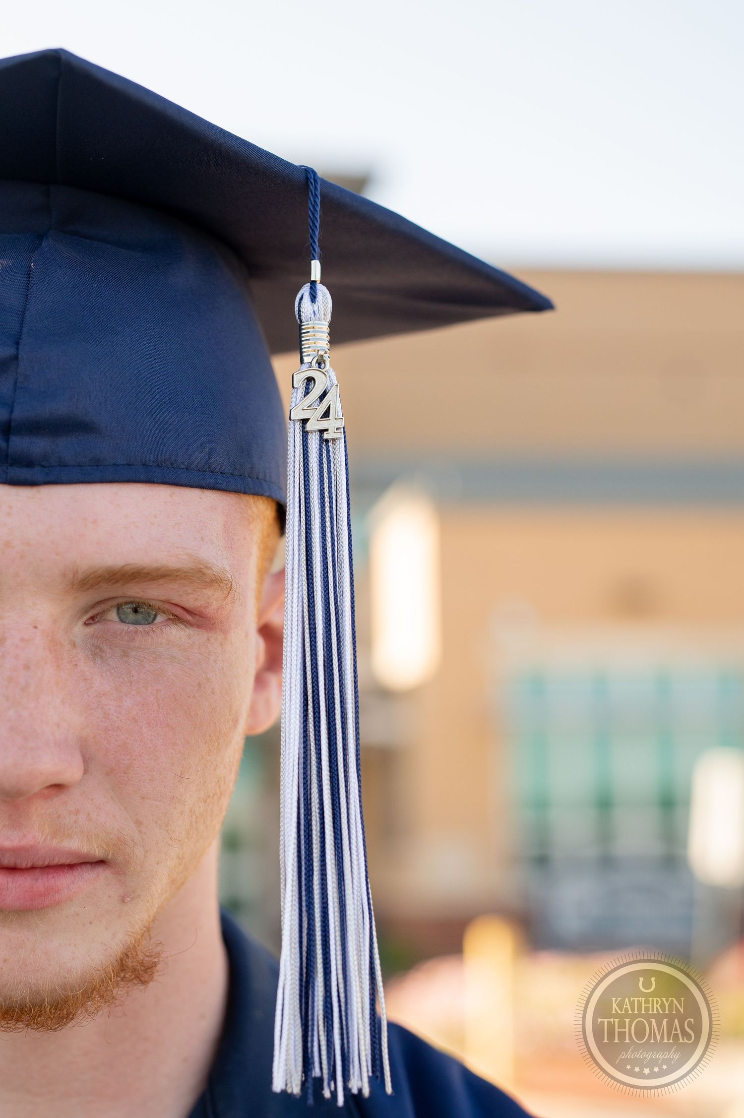 Close-up detail of graduation cap with silver tassel against brick building background.