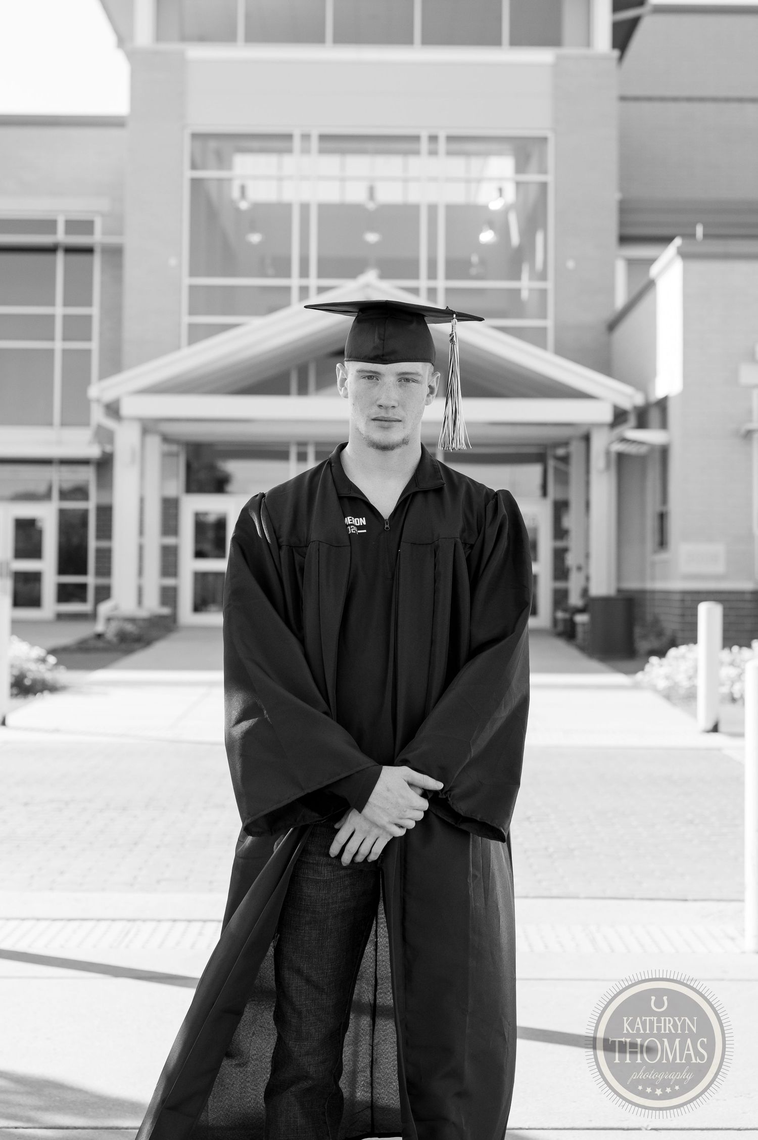 Black and white photo of graduate standing in academic regalia outside campus building.