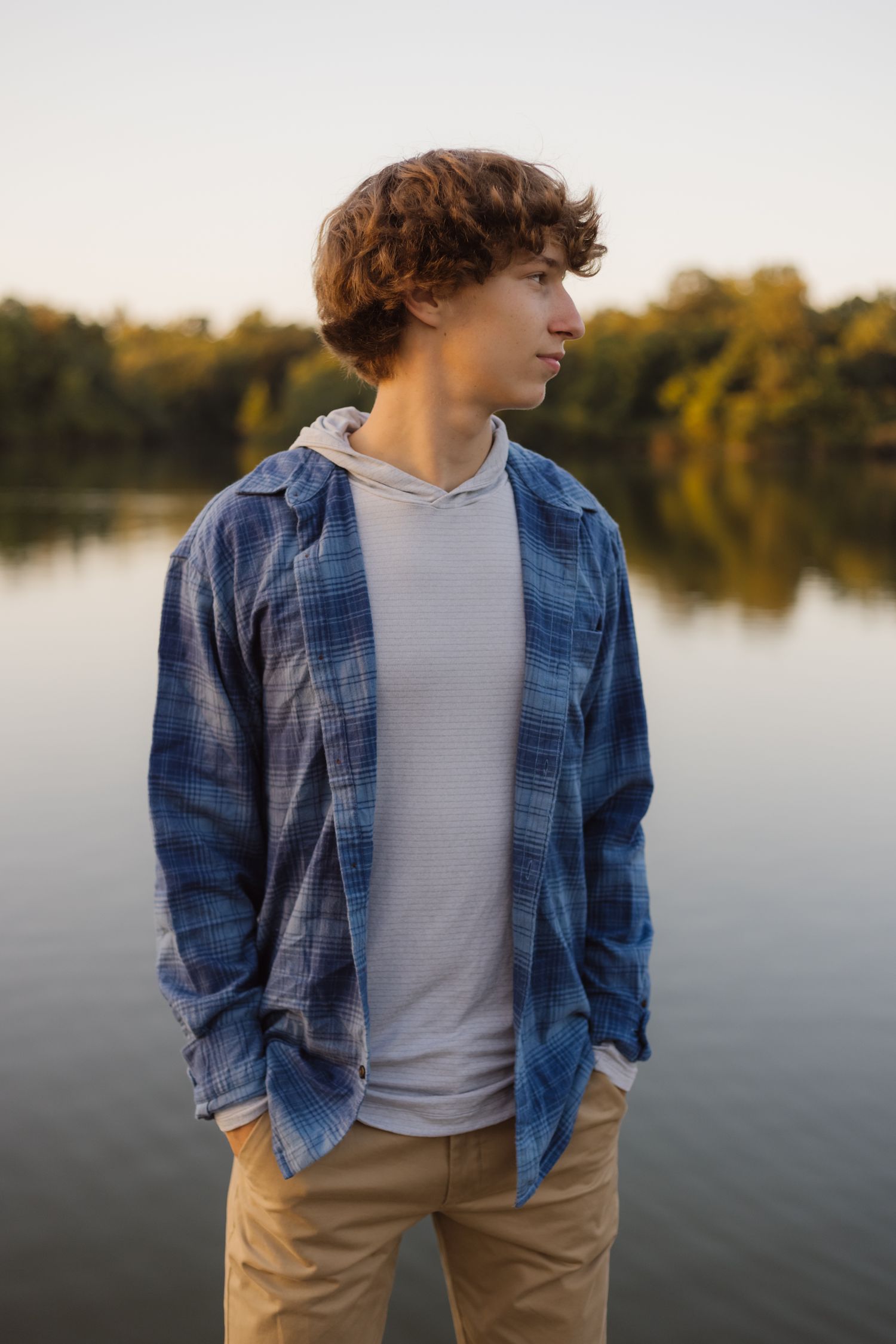 A lakeside portrait at sunset featuring someone in a blue plaid shirt and hoodie.