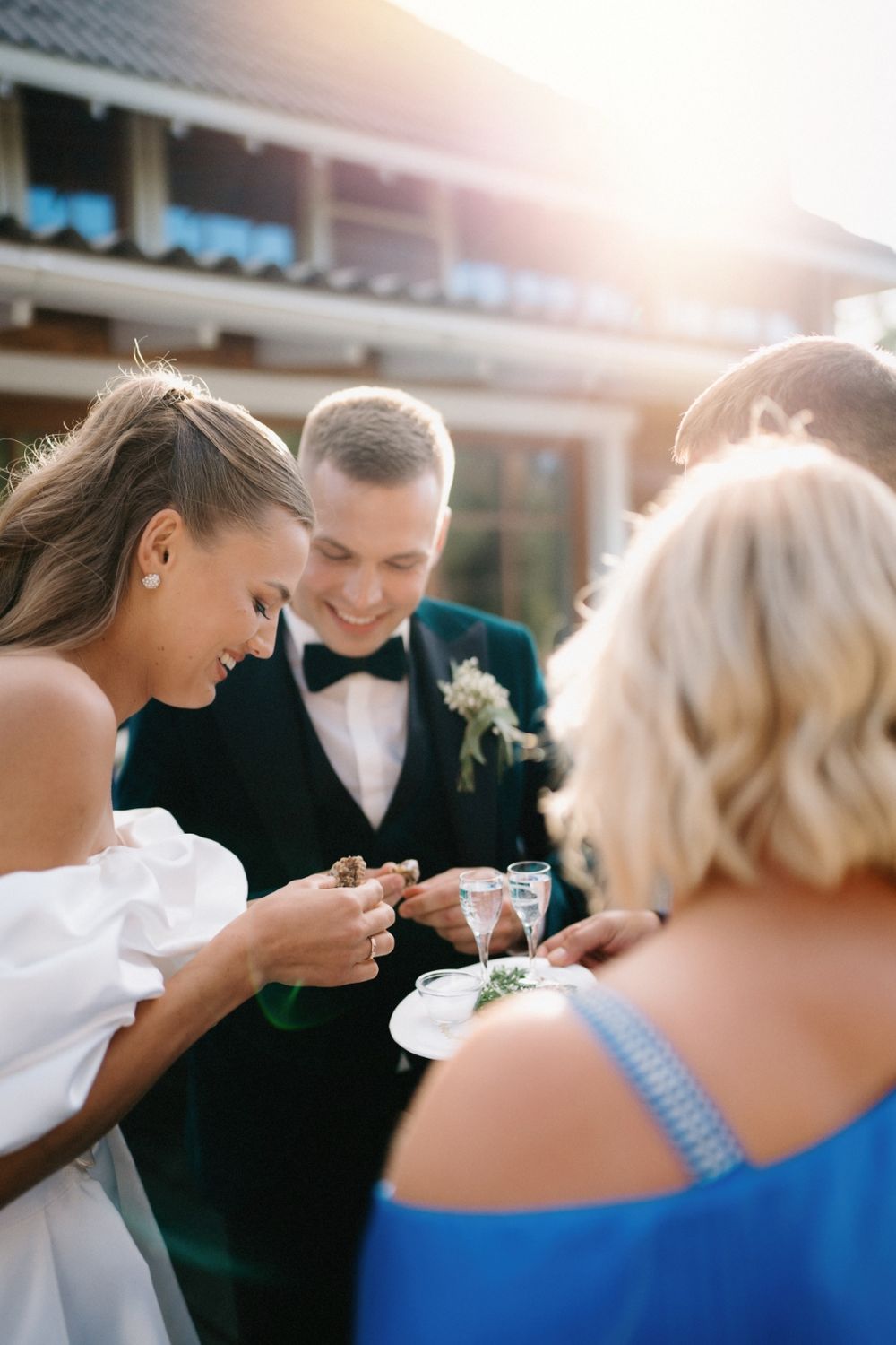 Wedding party members share intimate moments while taking shots during sunset reception.