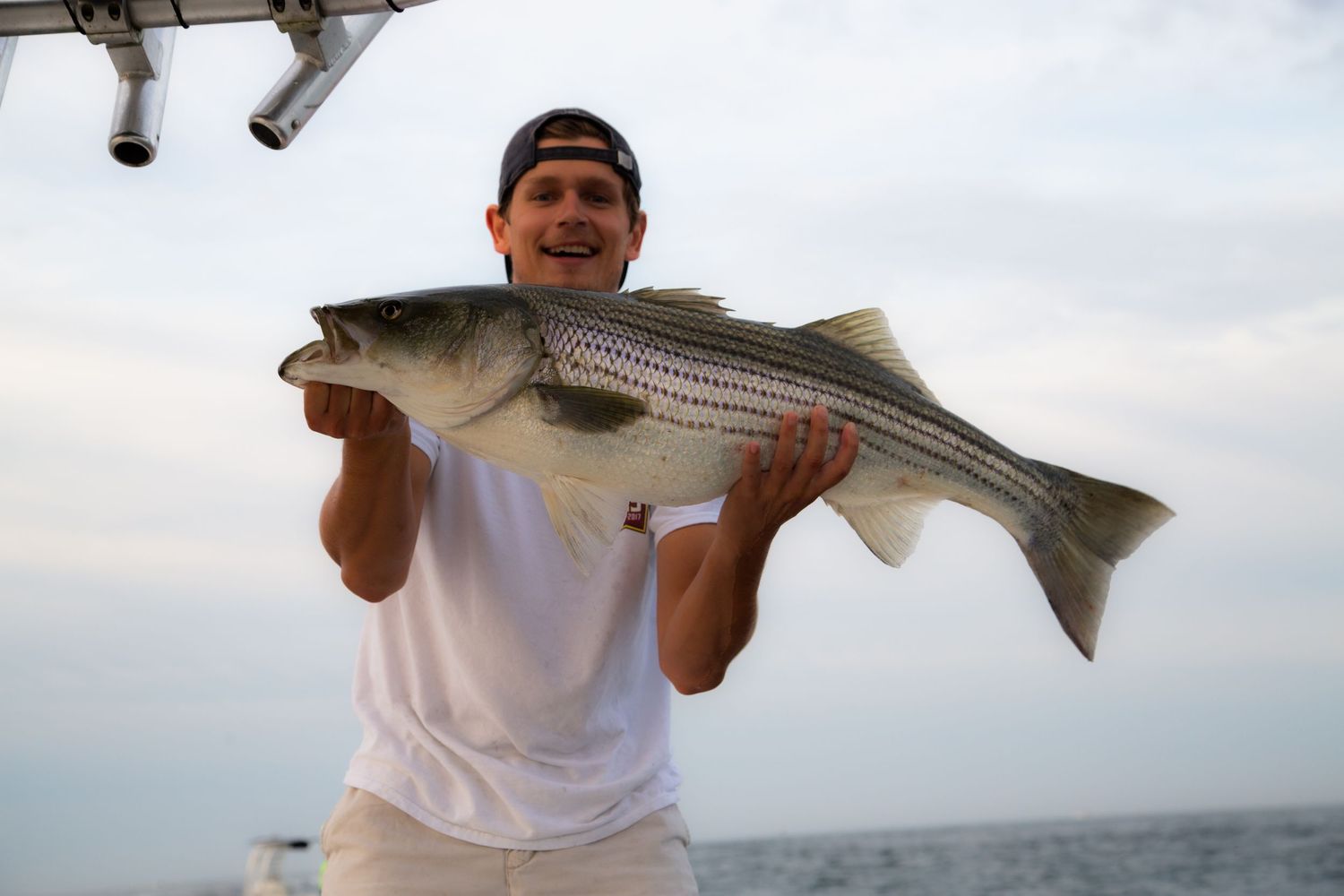 Proudly displayed striped bass catch held up against cloudy coastal sky.