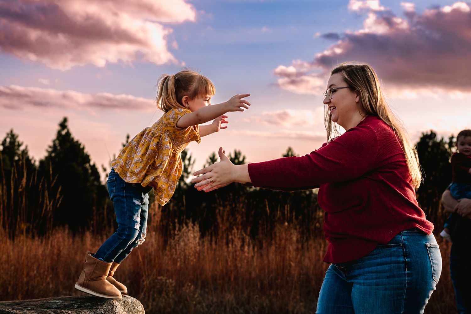 A joyful moment captured at sunset as a child leaps from a rock into welcoming arms.