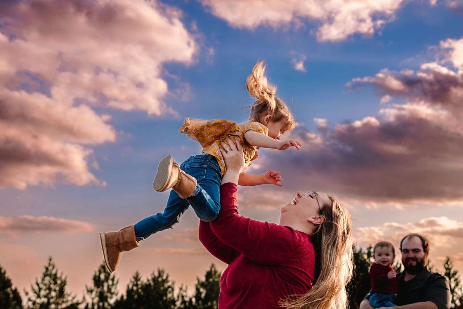 A playful moment captured against pink sunset clouds as a child is lifted into the air.