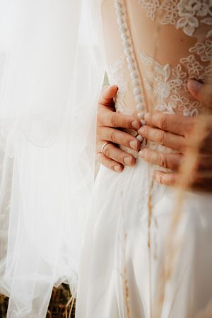 Close-up detail of delicate lace and hands on a wedding dress against soft white tulle fabric.