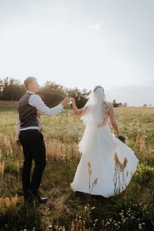 Joyful wedding couple dancing in golden sunset light among wildflowers.