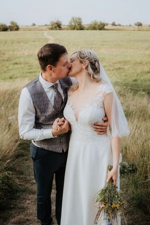 Intimate wedding couple moment in rustic field with vintage-inspired attire.