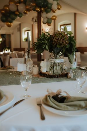 Elegant wedding reception table setting with greenery centerpiece and balloon arch.