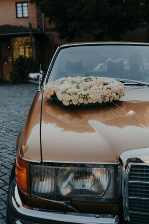 Vintage bronze Mercedes car decorated with white rose floral arrangement.