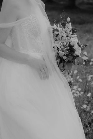 Black and white photograph of a wedding dress detail with a floral bouquet.