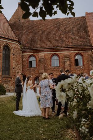 Wedding ceremony gathering outside historic brick church with gothic arched windows and red tile roof.