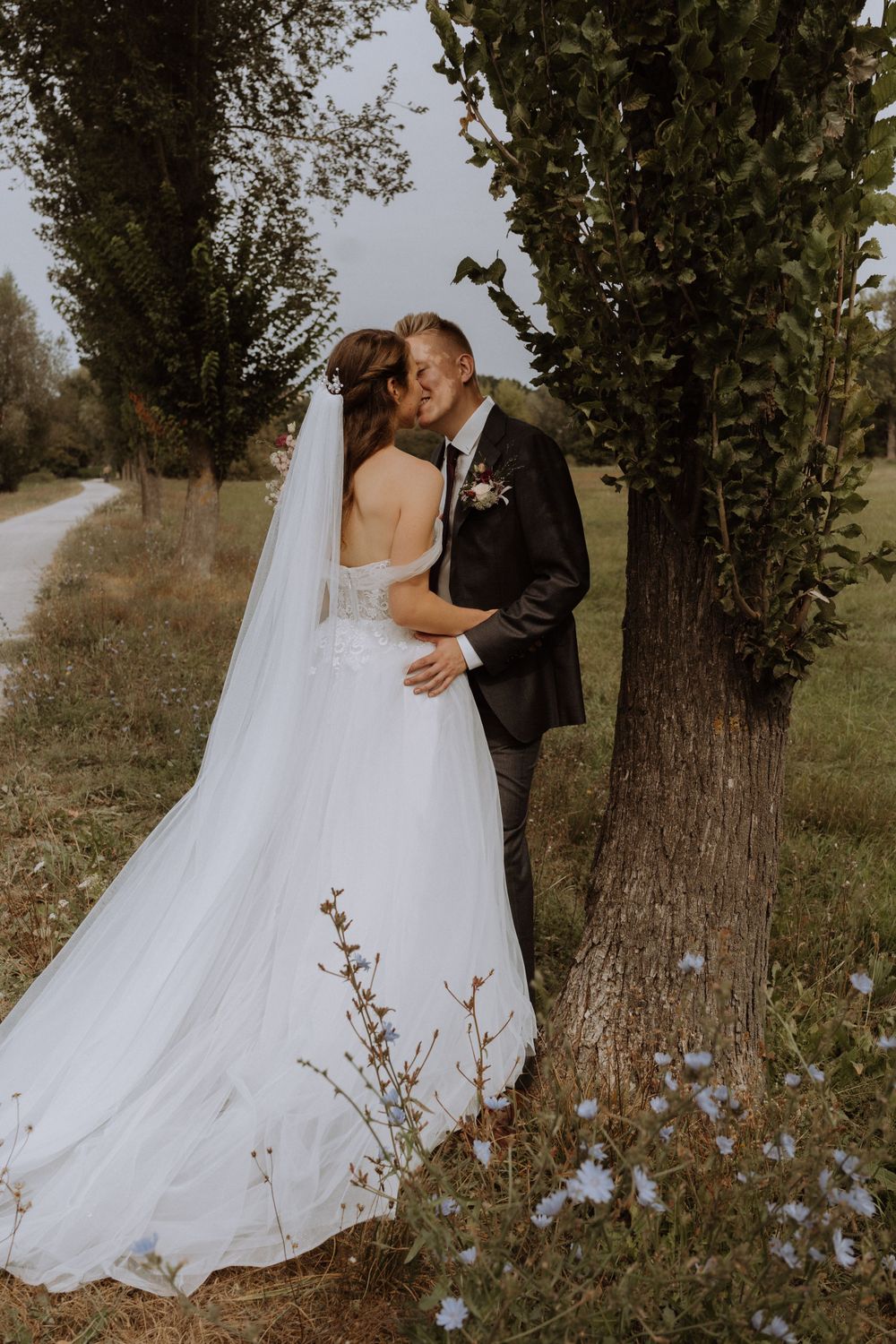 Romantic outdoor wedding portrait with white flowers and trees along a country path.