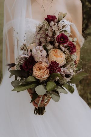 A stunning bridal bouquet featuring burgundy roses, peach garden roses, and white flowers.