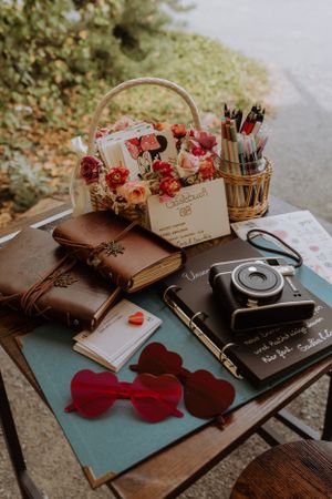 Vintage camera and journals with romantic floral arrangement and heart-shaped accessories on wooden surface.