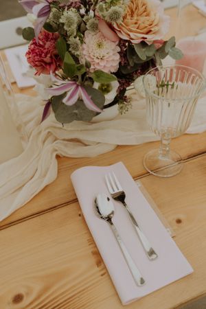 Wedding table decor with pink floral centerpiece, crystal glass, and white napkin on wooden surface.