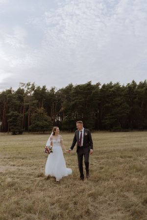 A romantic wedding couple walking hand in hand through a meadow with pine trees in the background.