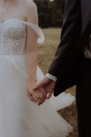 A close-up of newlyweds holding hands, with the bride wearing a detailed lace wedding dress.