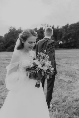 A bride in a white lace gown holds a beautiful bouquet while standing in a field.