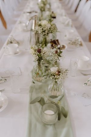 Elegant wedding table setting with delicate white flowers in glass vases and white linens.