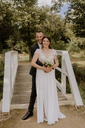 Wedding portrait on white wooden bridge surrounded by lush green trees.