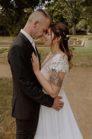 Tender wedding moment captured in natural outdoor setting with lace dress details.