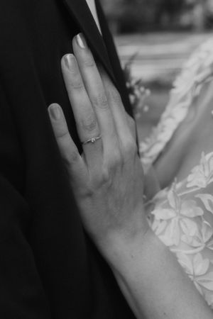 Close-up black and white photo of a delicate hand with a wedding ring resting on fabric.