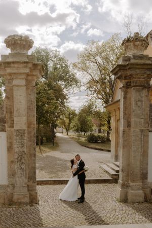 Romantic embrace between stone pillars at an ornate entrance gate.