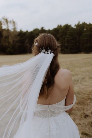 Back view of a bride's hairstyle with floral details and flowing veil against a natural backdrop.