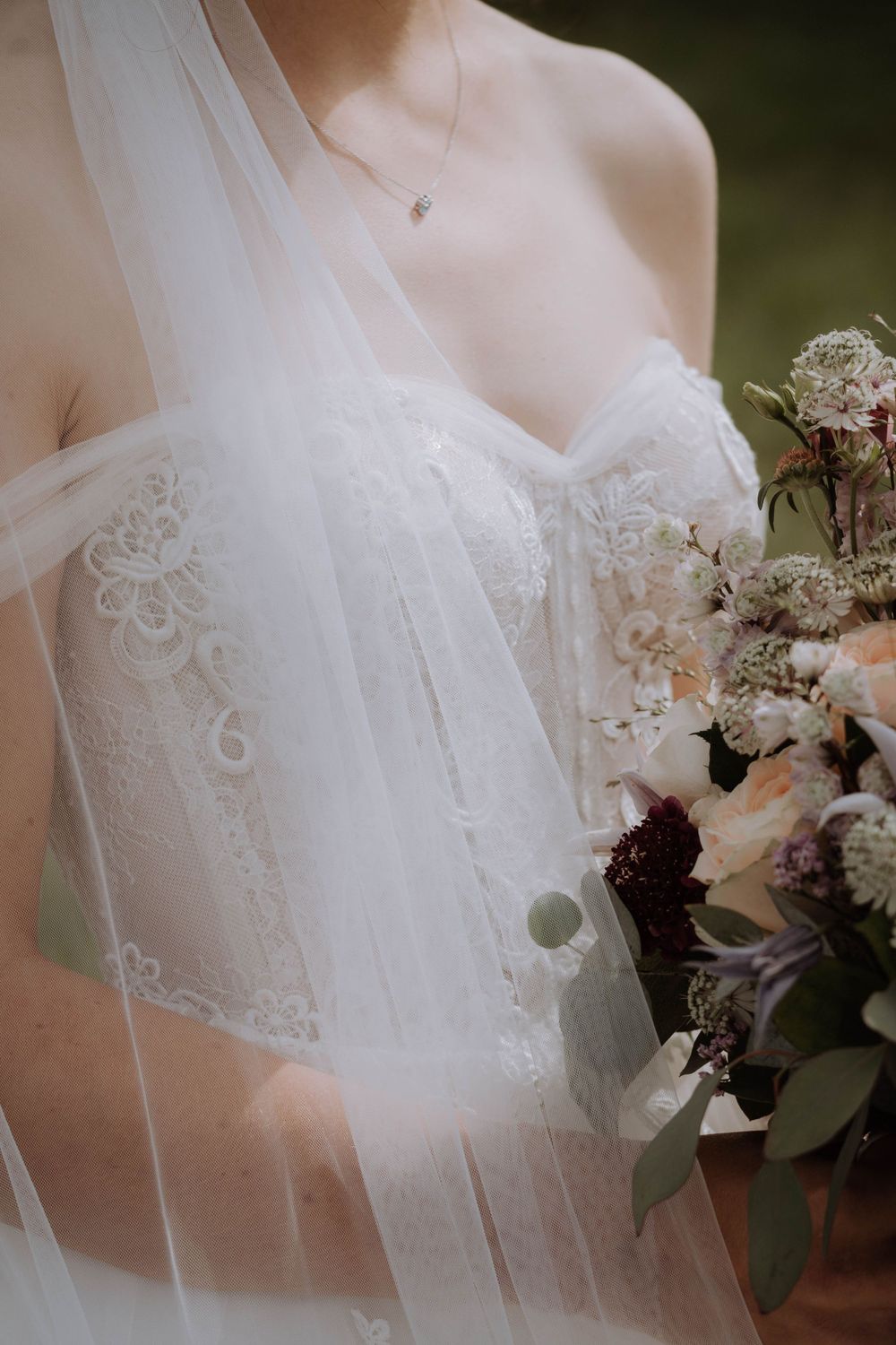 A delicate white lace wedding dress bodice with veil and floral bouquet details.
