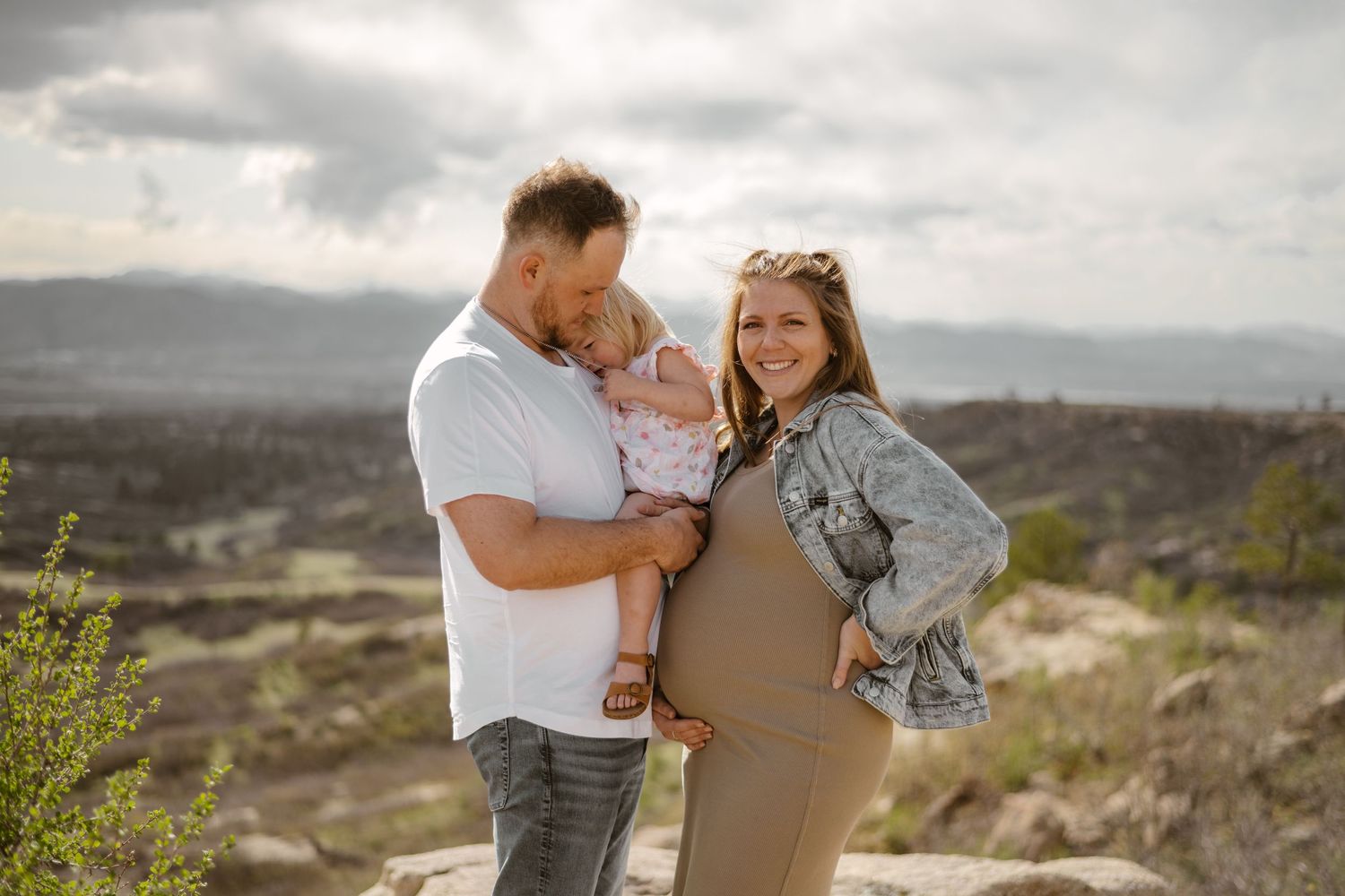Couple embracing on desert cliff with dramatic cloudy sky backdrop.