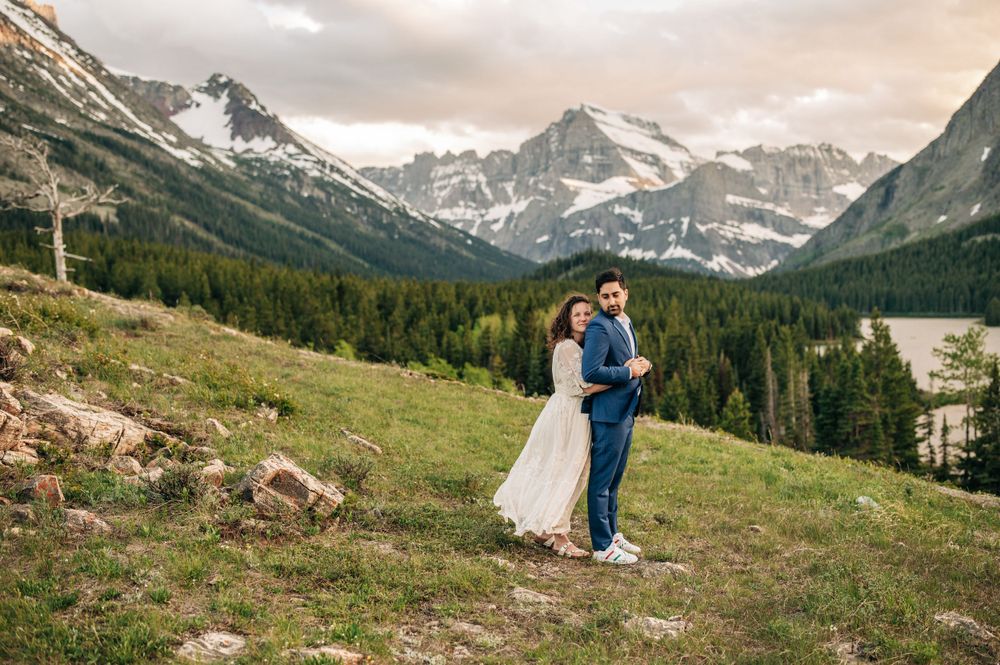 wedding couple, hugging, mountains and lake behind them in glacier national park