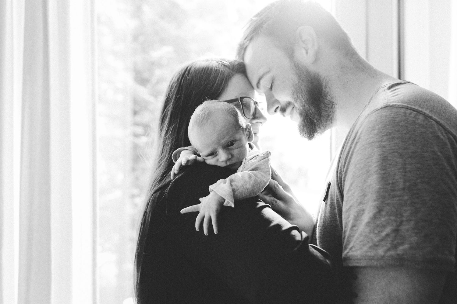 Paar schaut sich verliebt an, während es sein neugeborenes Baby im Wochenbett hält