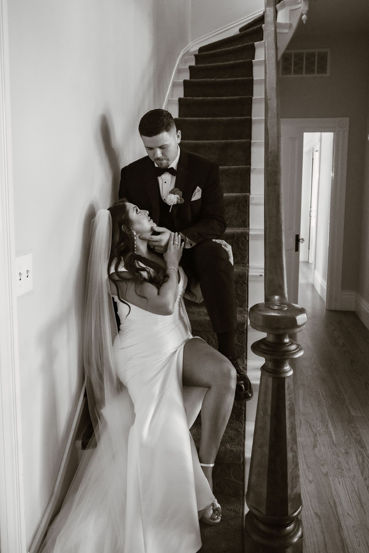 Black and white wedding photo showing romantic moment on vintage wooden staircase.