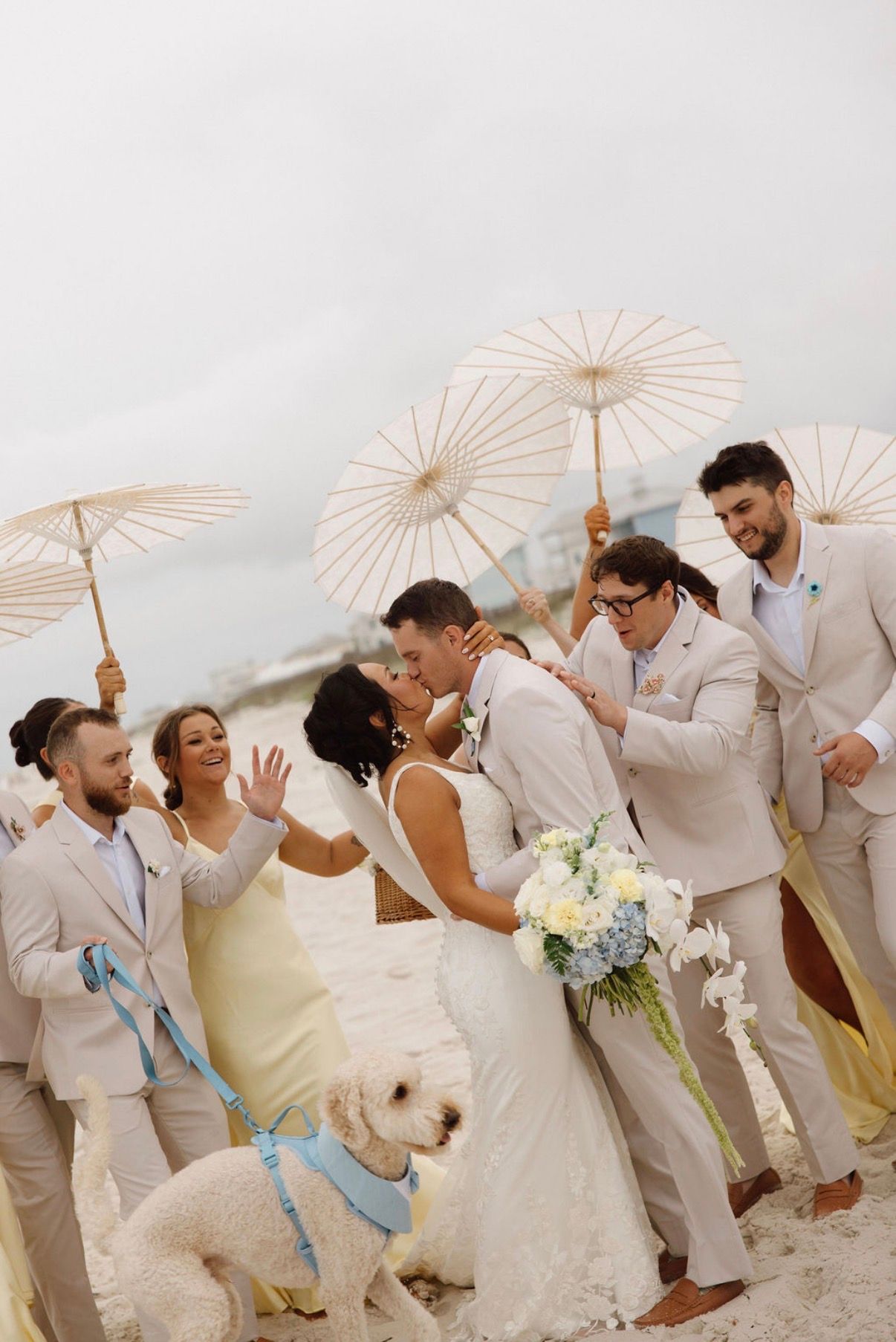 Wedding party celebrates joyfully outdoors wearing light colored suits and dresses.